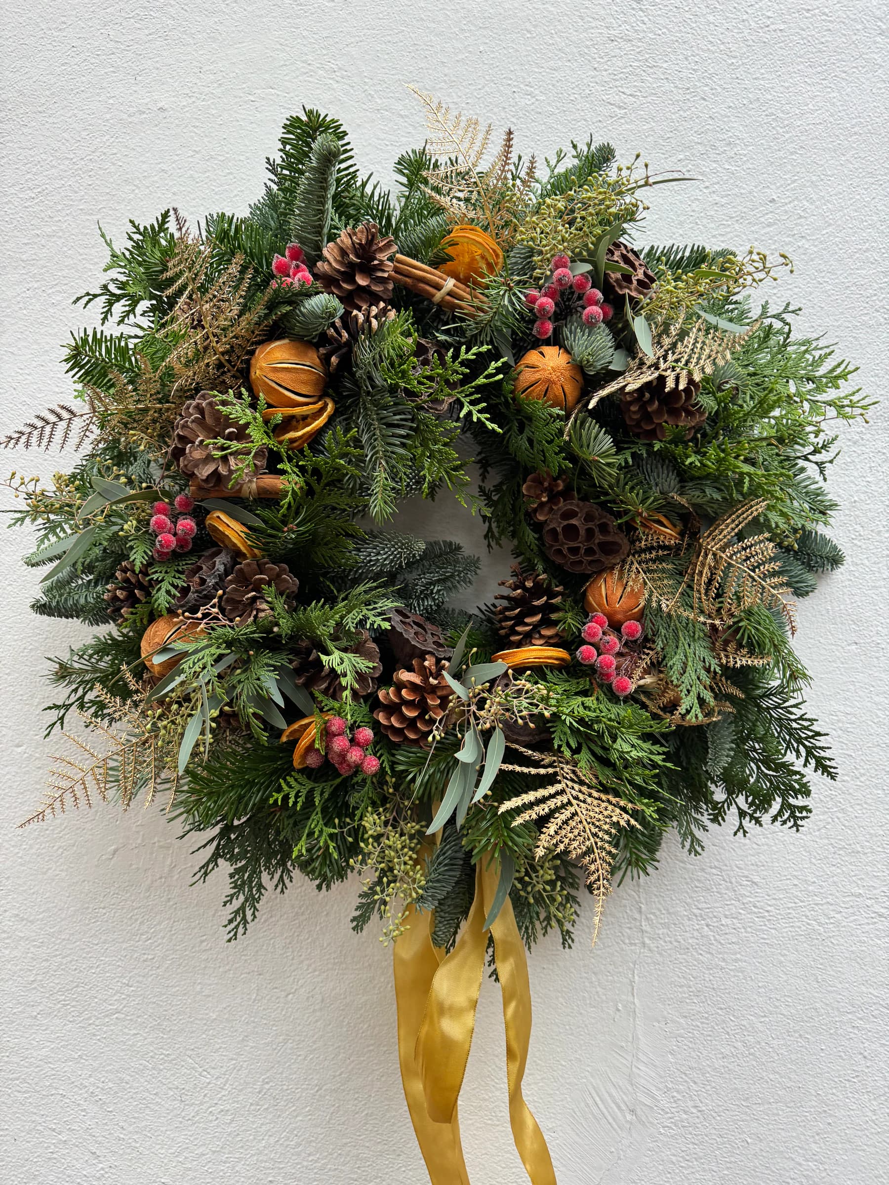A fresh Christmas wreath with dried oranges, berries, cones and a gold ribbon