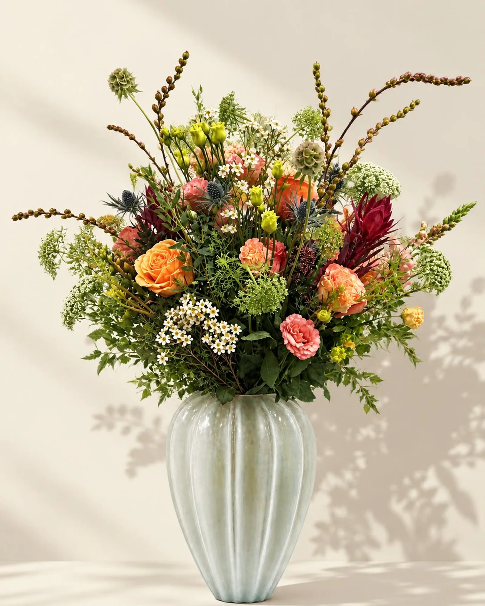 Autumn Glory — burnt-orange roses, leucadendron, scabious seed heads and ammi in a fluted celadon vase, on warm linen