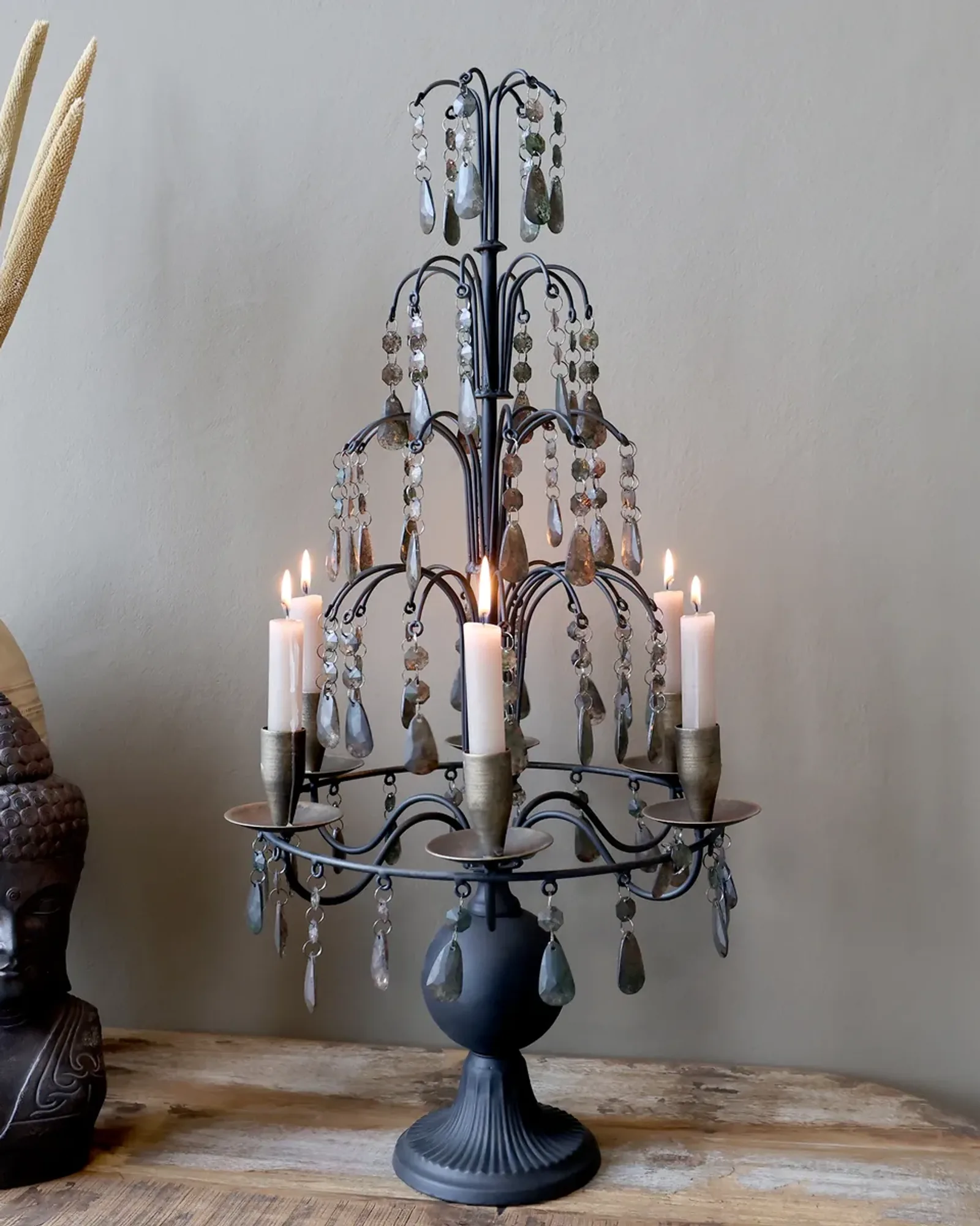A tall tiered dark-brown iron candelabra with five candle cups and hanging smoky prisms on a fluted base, standing on a table.