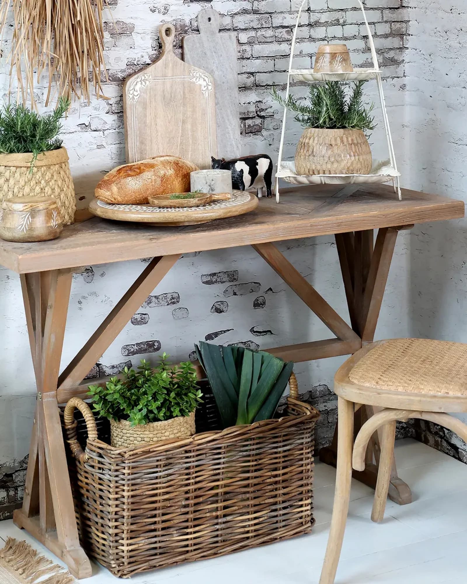 A narrow natural recycled-wood table with X-shaped trestle legs, laid with bread, boards and baskets.