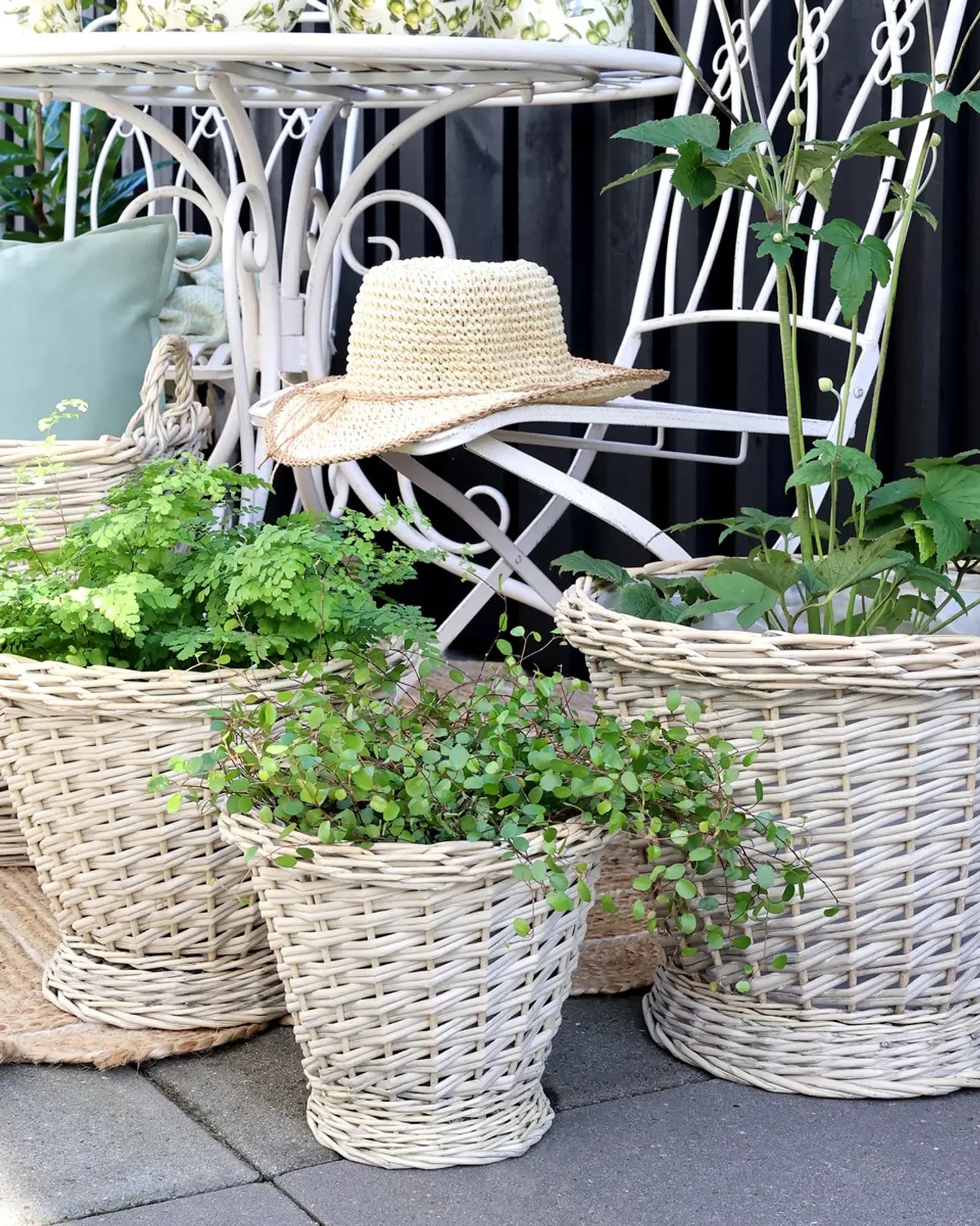 Three tapered pale willow baskets in small, medium and large sizes, planted up, on a garden table.