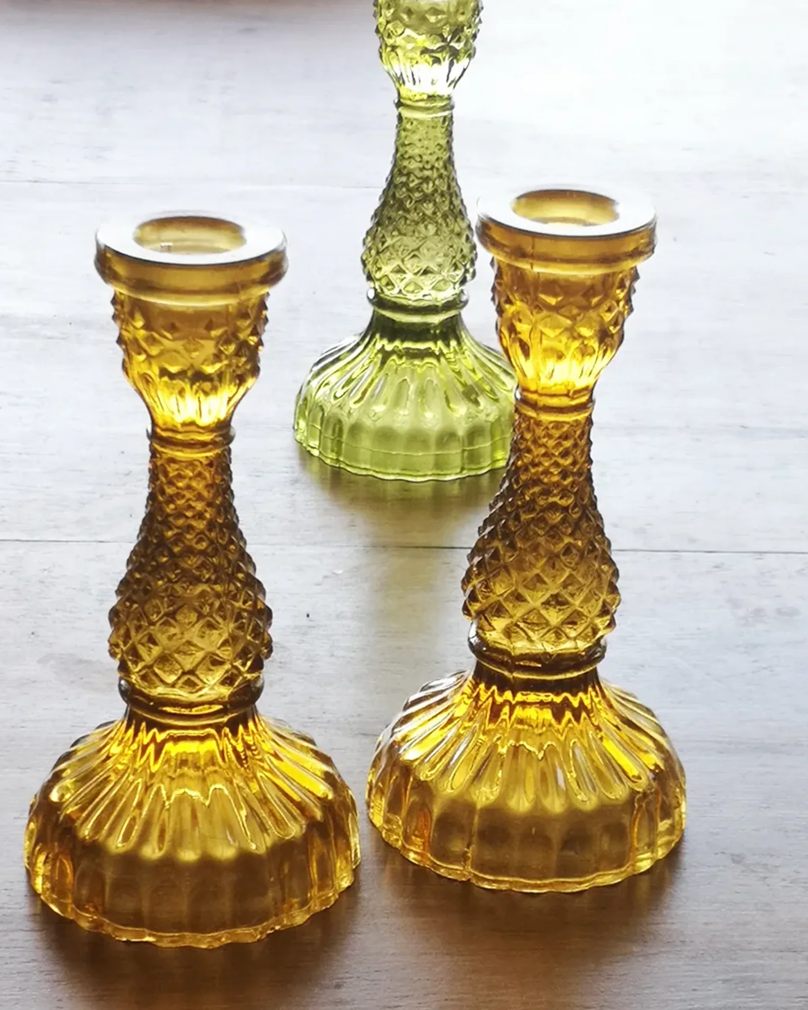 A tall amber glass candlestick holding an unlit dinner candle, photographed on its own.