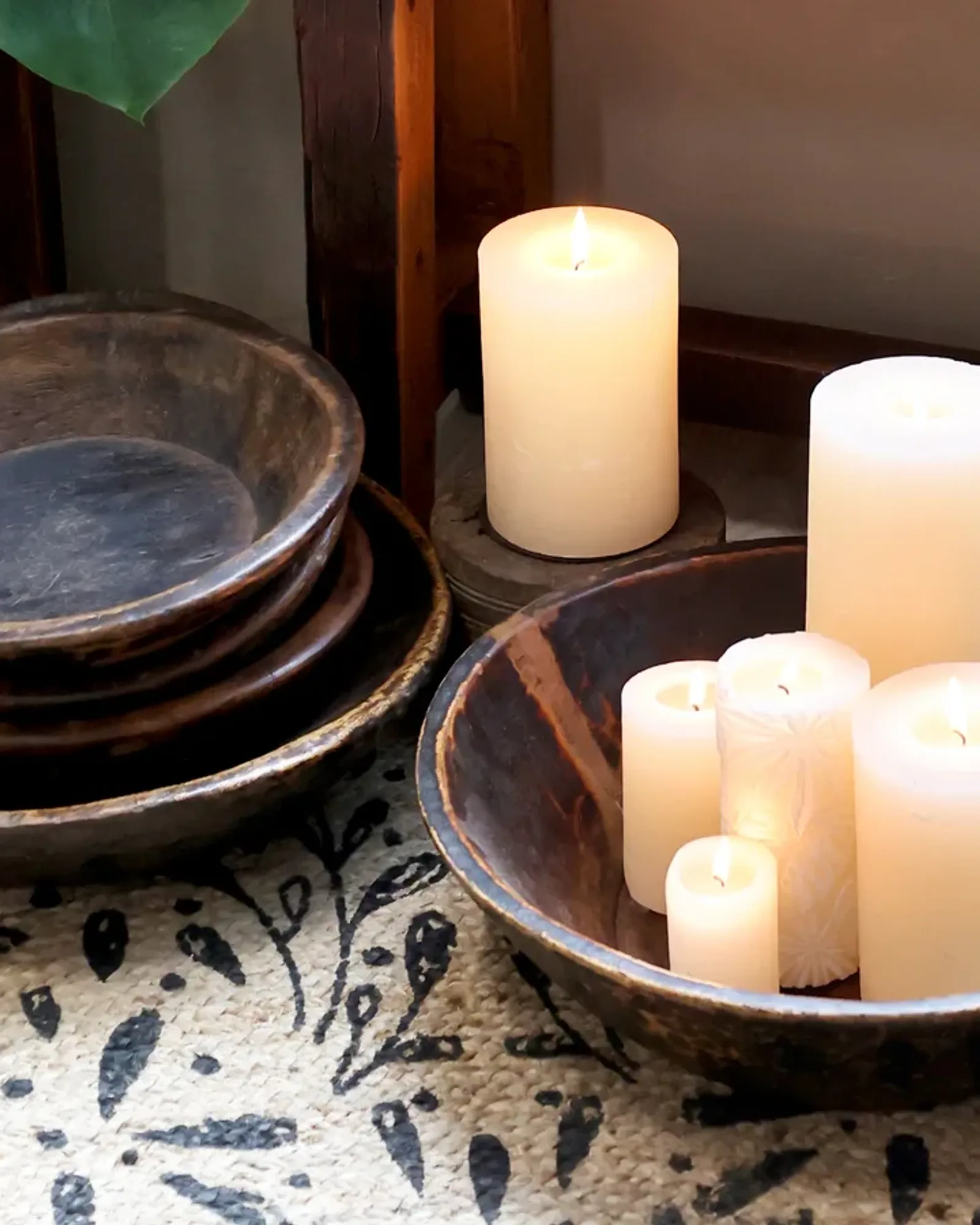 A stack of shallow round recycled-wood trays in several sizes, the top one holding candles.