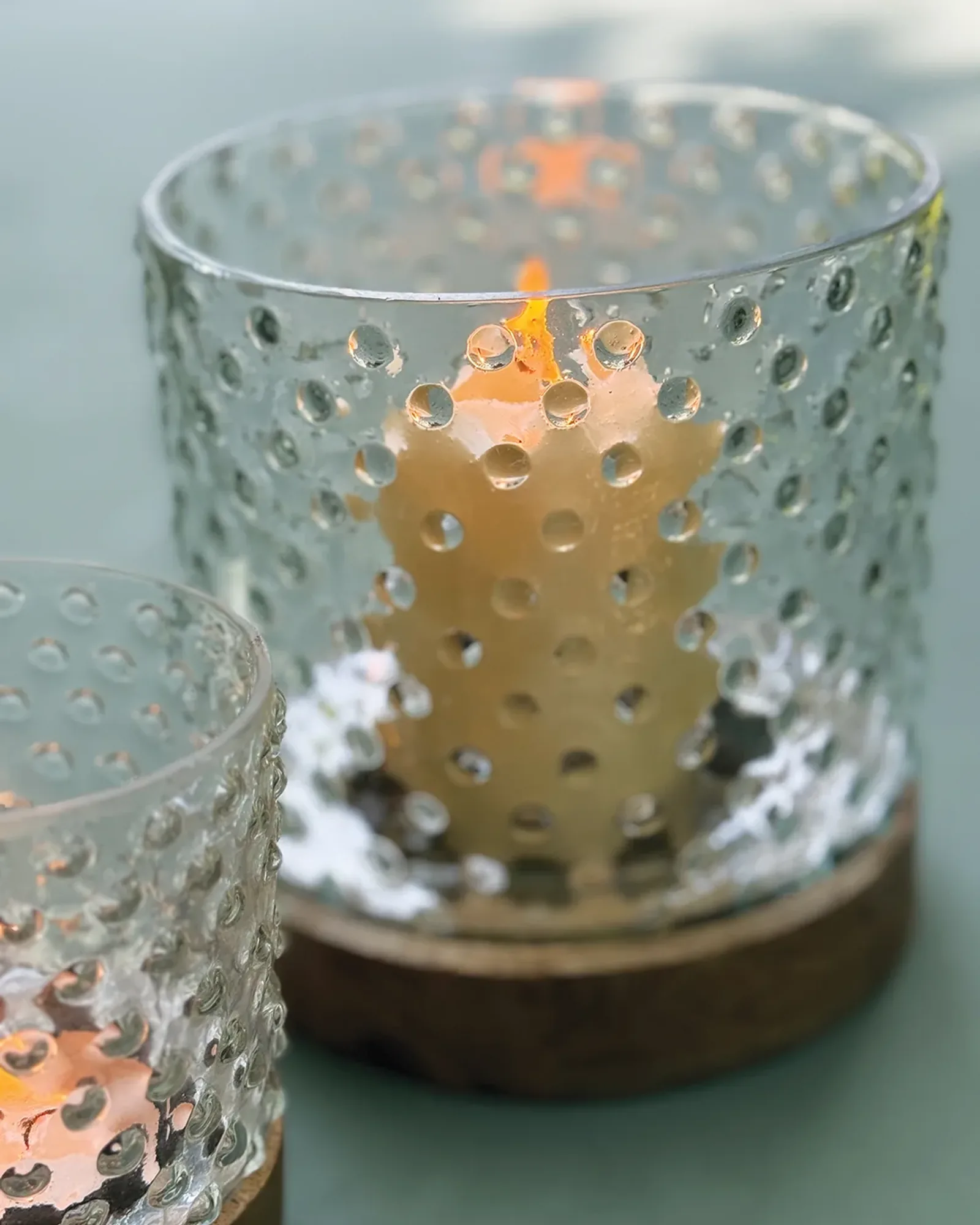 A glass hurricane patterned with polka dots on a round wooden base, holding a small candle.