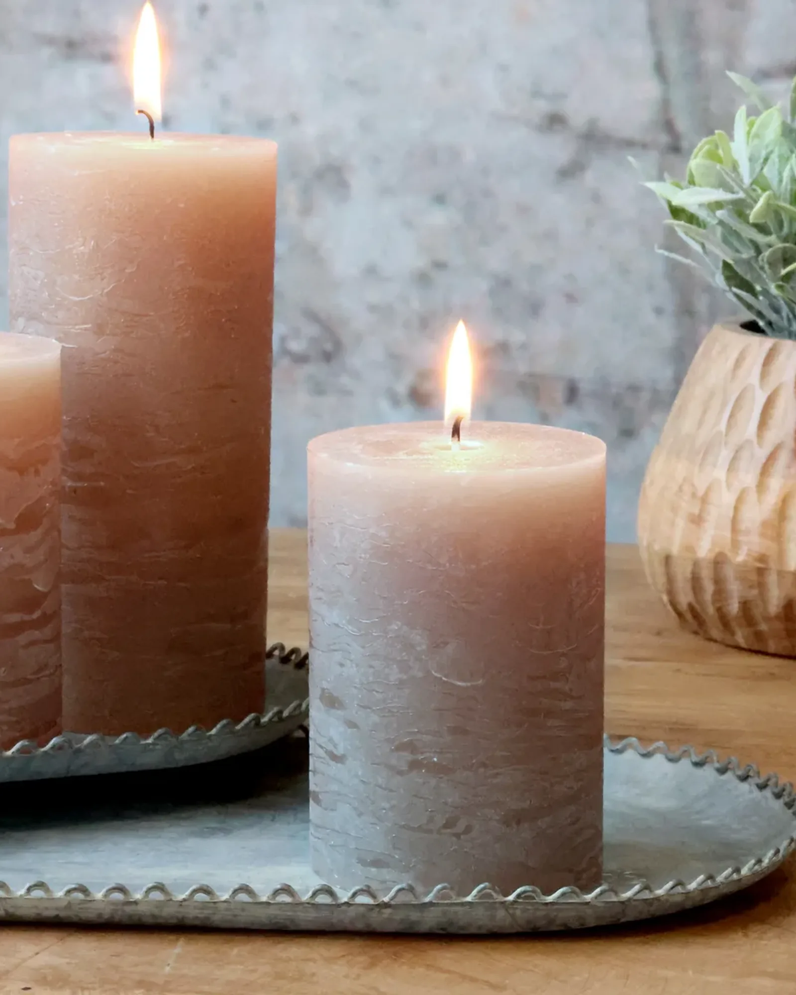 Three rustic pillar candles in different greige shades on a zinc tray.