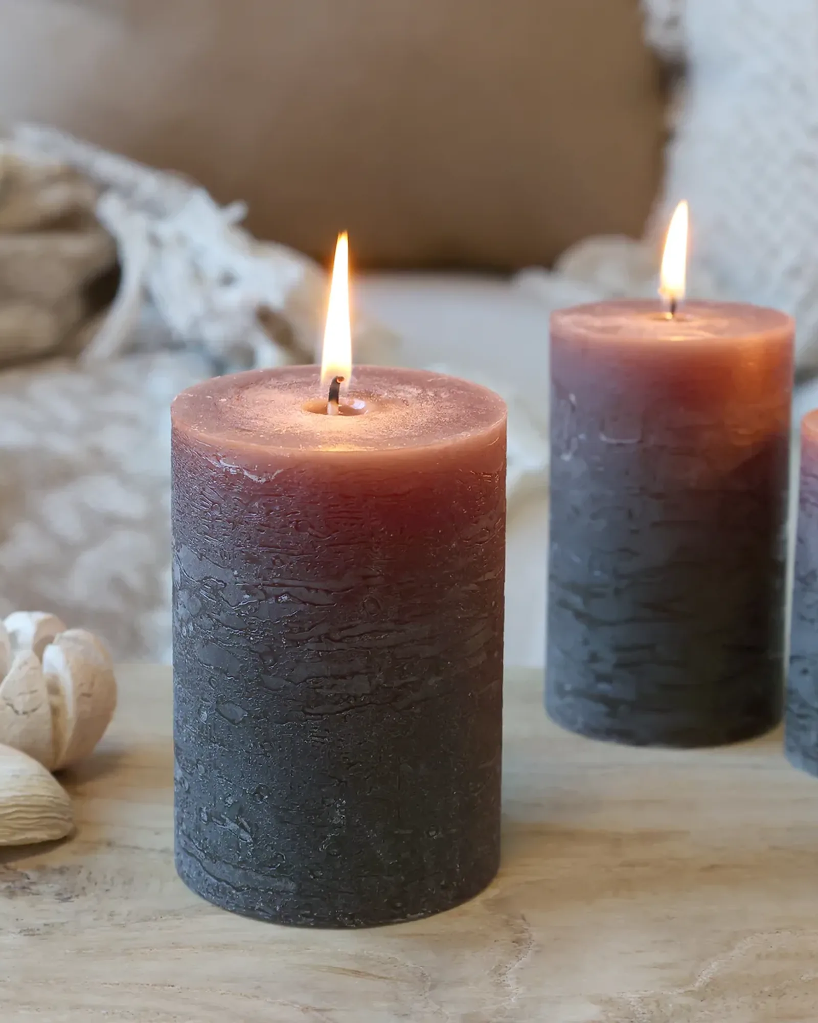 A short rustic pillar candle in coffee brown, lit, with taller candles of the same colour behind it.