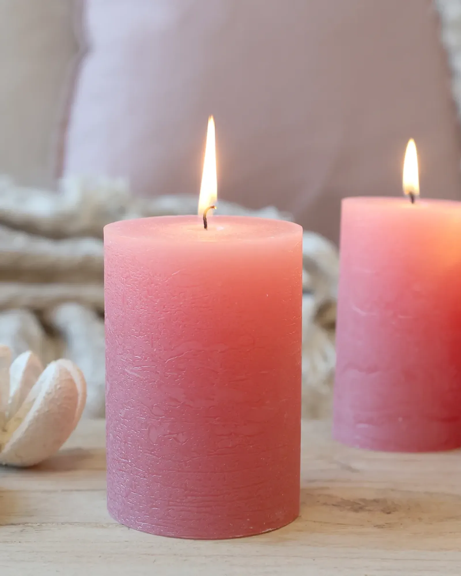 A short rustic pillar candle in raspberry pink, lit, with taller candles of the same colour behind it.
