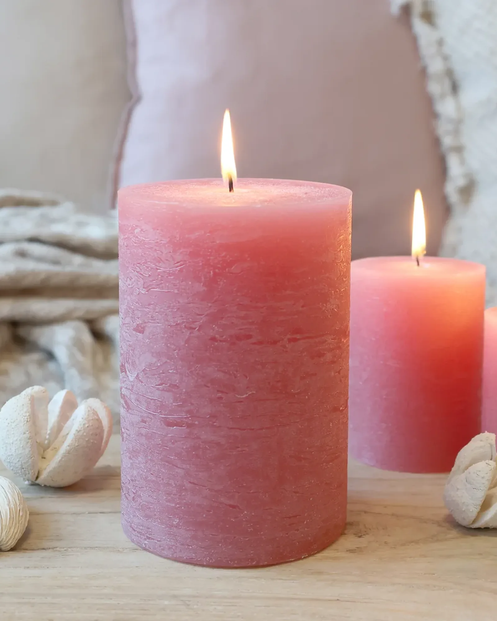 A wide rustic pillar candle in raspberry pink, lit, with smaller candles of the same colour behind it.