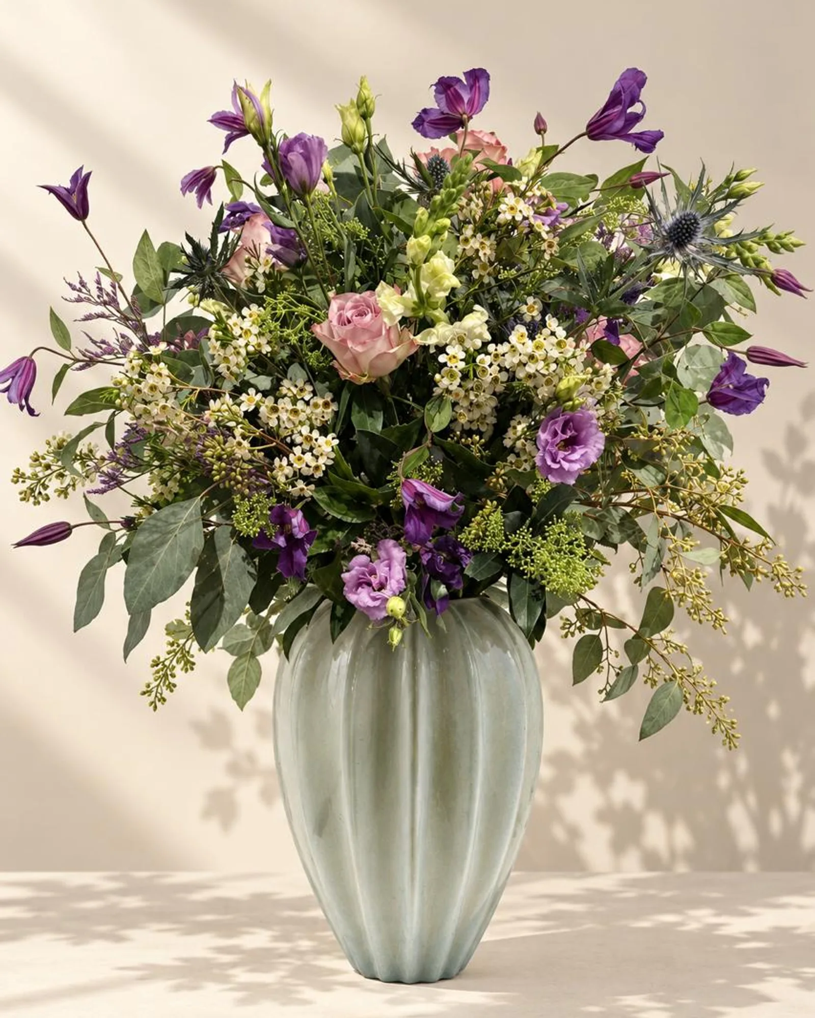 Memory Lane — lilac roses, purple campanula, lisianthus and eucalyptus in a fluted celadon vase, on warm linen