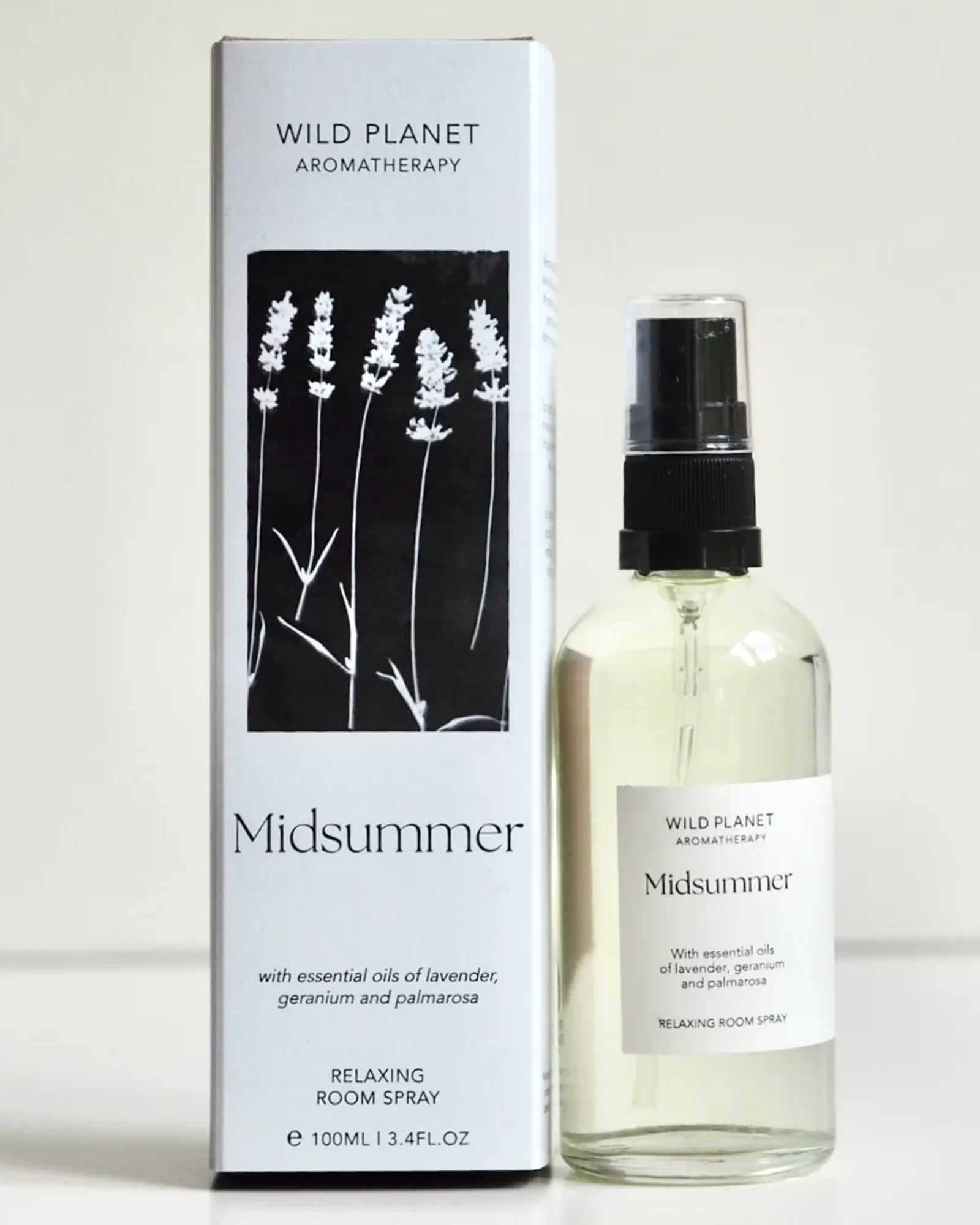 A clear glass bottle of Midsummer room spray with a black spray pump and a small cream label naming the scent.