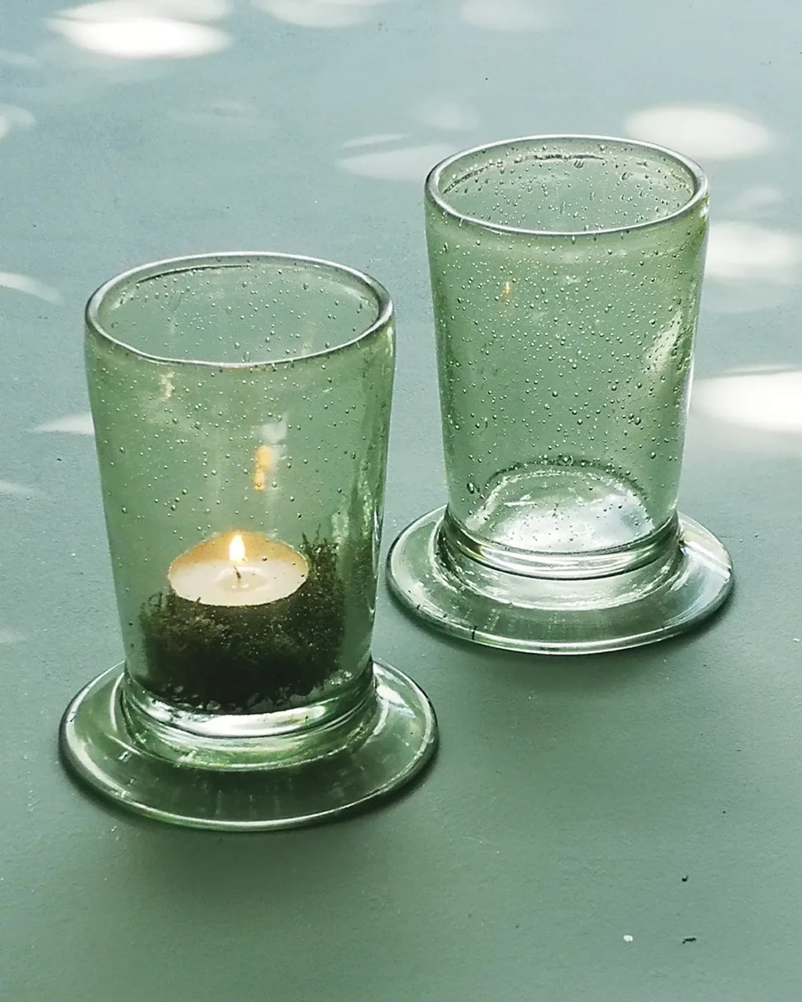A small glass hurricane with a rustic finish, holding a lit tealight, photographed on a table.