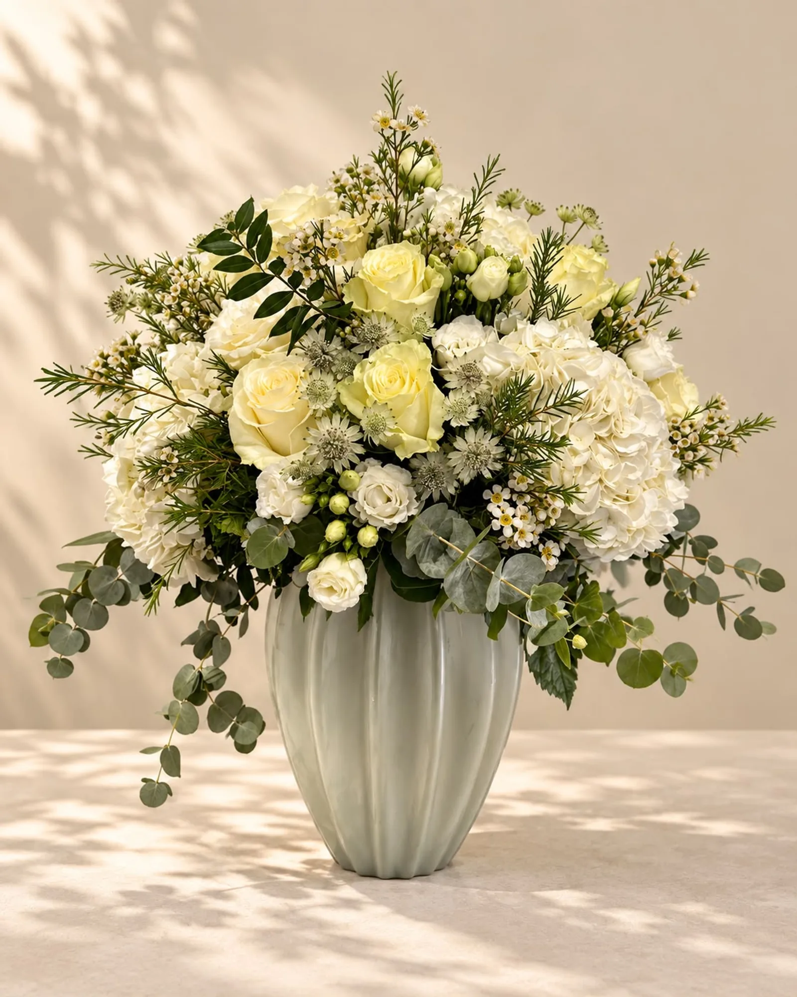 Pure Luxury — cream roses, white hydrangea and eucalyptus in a fluted celadon vase, on warm linen