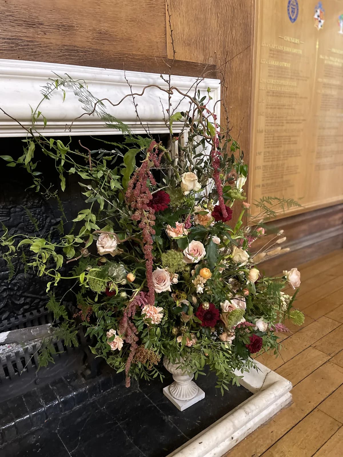 A loose urn arrangement of garden roses and amaranthus in a marble fireplace