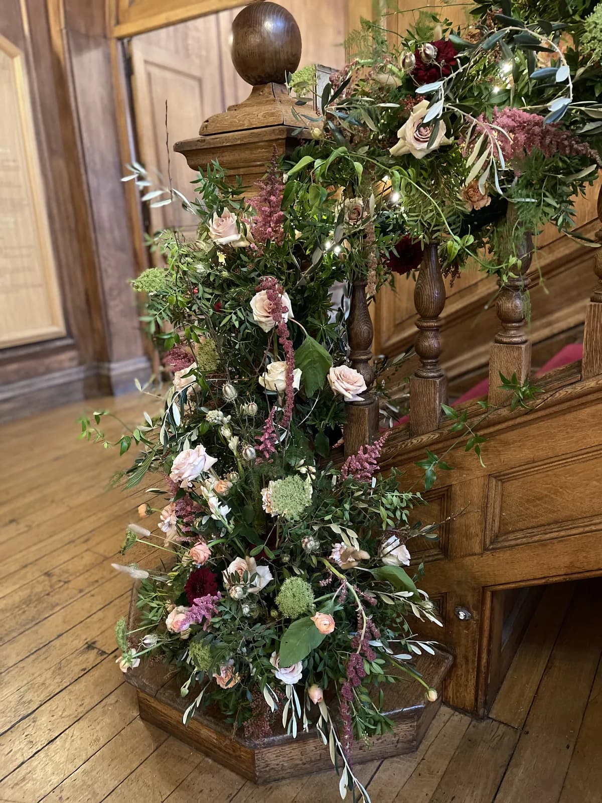 A foliage and garden-rose installation climbing the newel post of an oak staircase