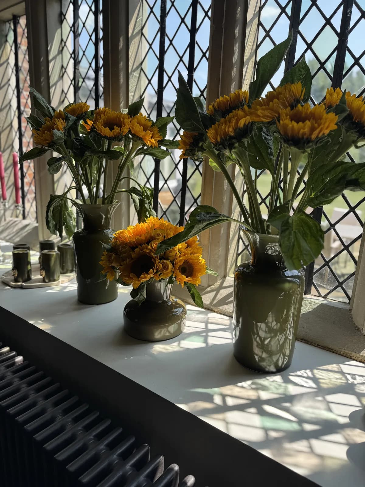 Sunflowers in olive-green vases along a leaded window sill