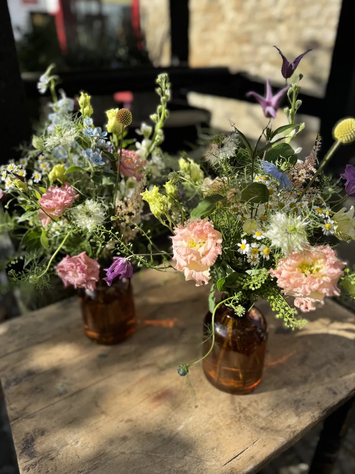 Two amber-glass bud vases of loose wildflower posies on a scrubbed wooden table