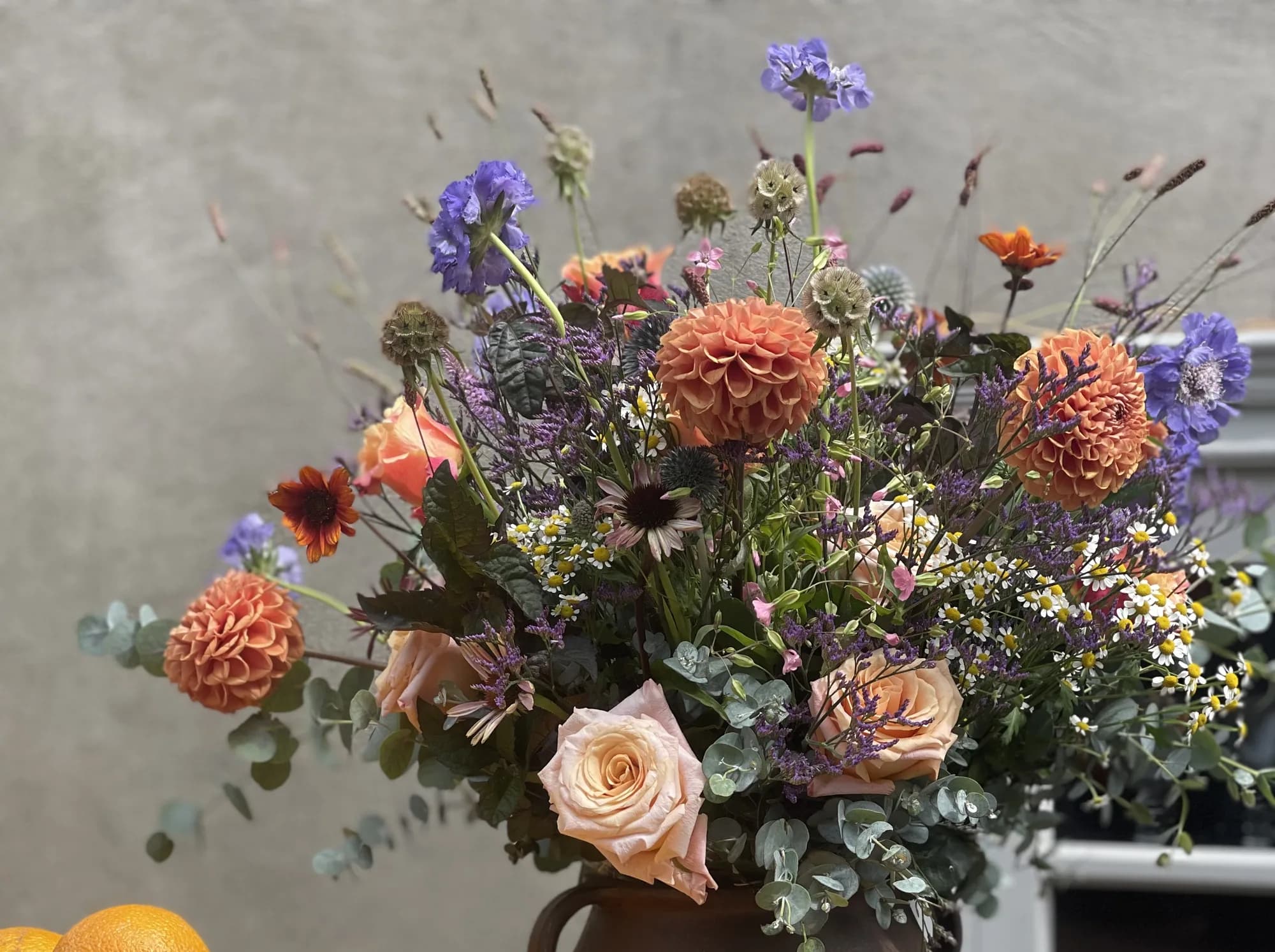 Orange dahlias and peach garden roses against a grey wall
