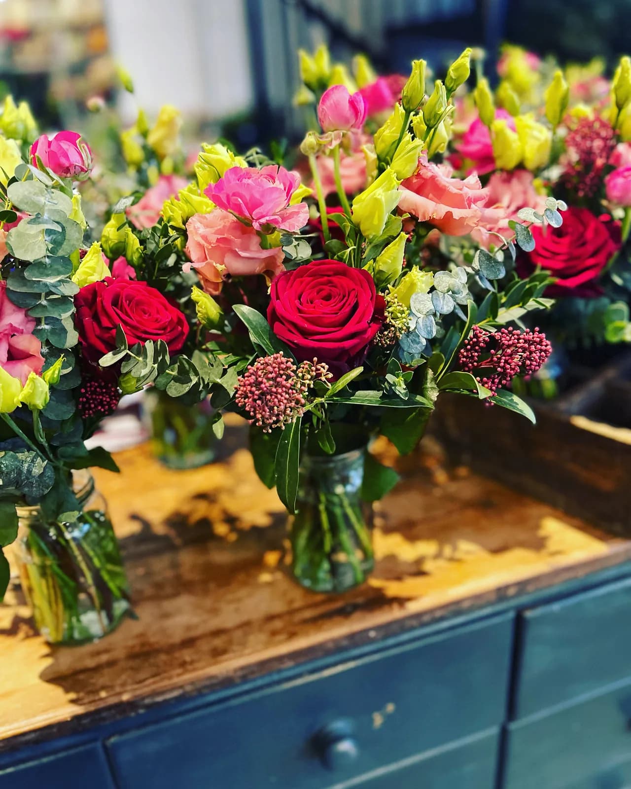 Jam-jar posies of roses, lisianthus and eucalyptus lined up on the studio counter