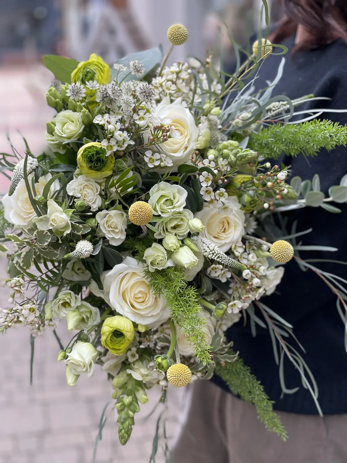 A hand-tied bridal bouquet of cream roses, ranunculus, craspedia and waxflower